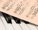 Partytura muzyczna z nutami, leżąca na klawiaturze fortepianu. Może to być utwór JS Bacha, gotowy do zagrania.