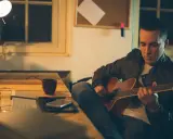 Mężczyzna gra na gitarze, ćwicząc skale gitarowe przy biurku.