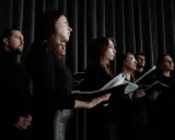 Chór w czarnych strojach, z nutami w rękach. Słychać głosy męskie i kobiece, tworzące harmonijną całość.