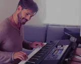 Uśmiechnięty mężczyzna gra na keyboardzie Yamaha, korzystając z aplikacji yamaha flowkey. Obok stoi mikrofon i głośnik.