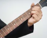 Dłoń dociska struny na gryfie gitary, pokazując pierwszy krok, jak nauczyć się grać na gitarze.