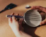 Ręce składają instrumenty perkusyjne: patyczek z ozdobnym papierem i miseczka z gumkami.