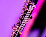 Zbliżenie na klarnet, piękny instrument dęty drewniany, z błyszczącymi klapami na tle fioletowo-różowego światła.
