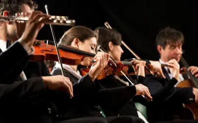 Orkiestra wykonuje utwór jednego z kompozytorów XX wieku. Skupieni muzycy grają na skrzypcach i wiolonczeli.