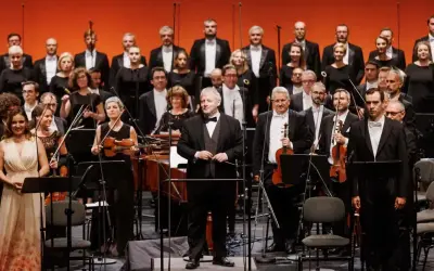 Orkiestra i chór przygotowują się do wykonania pieśni Moniuszki. Dyrygent stoi na podwyższeniu, muzycy trzymają instrumenty.