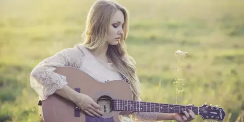 Dziewczyna gra na gitarze, tworząc piękny riff. Słońce delikatnie oświetla jej blond włosy i koronkową sukienkę.