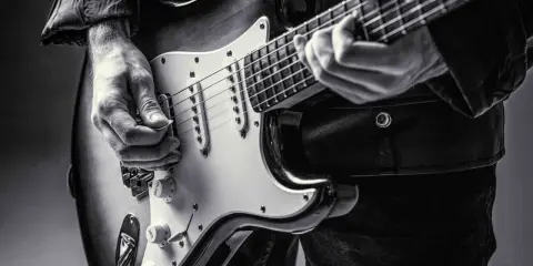 Ręce muzyka grające na gitarze do metalu. Czarno-białe ujęcie z bliska.