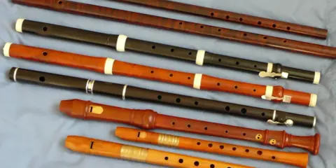 Różnorodne instrumenty renesansu, w tym flety proste o różnych rozmiarach i materiałach, ułożone na niebieskim tle.
