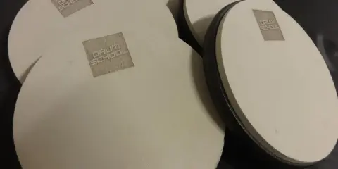 Kilka okrągłych, beżowych padów perkusyjnych z logo "DRUM SCHOOL" leży na czarnym tle.