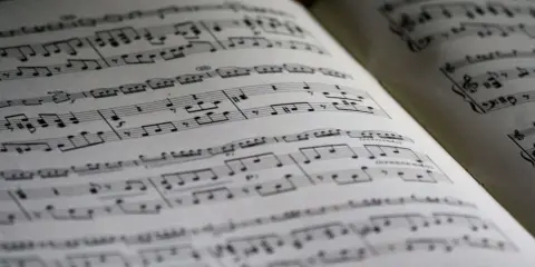 Otwarta księga z nutami na pięciolinii. Czarno-białe zapisy muzyczne wypełniają strony, czekając na wykonanie.