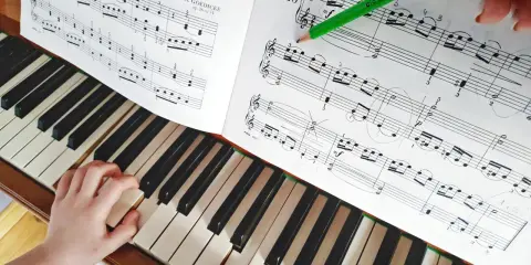 Dziecko uczy się grać na pianinie, ćwicząc nuty z podręcznika. Zielony ołówek wskazuje fragment partytury, co ułatwia naukę gry na instrumentach dla dzieci.