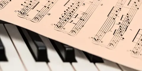 Partytura muzyczna z nutami, leżąca na klawiaturze fortepianu. Może to być utwór JS Bacha, gotowy do zagrania.