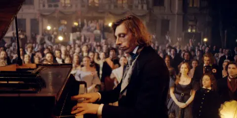 Młody Fryderyk Chopin gra na fortepianie przed zgromadzoną publicznością.