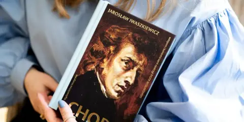 Kobieta trzyma książkę o Chopinie. Portret kompozytora na okładce. Piękna muzyka Chopina.