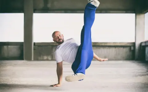 Mężczyzna w białej koszulce i niebieskich spodniach wykonuje akrobatyczny ruch. Czy to może być odpowiedź na pytanie: beatbox co to?