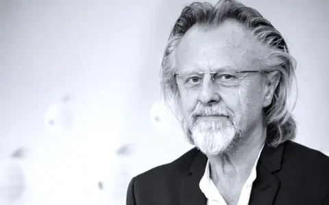 Portret mężczyzny z siwą brodą i długimi włosami, w okularach. Jeden z najlepsi współcześni kompozytorzy.