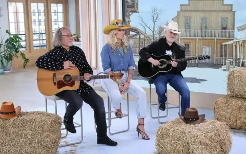 Trzech muzyków gra na gitarach, tworząc muzykę country. W tle stylizowana scenografia z Dzikiego Zachodu.