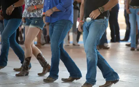 Ludzie w dżinsach i kowbojkach tańczą w rytm amerykańskiego country.