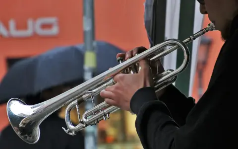 Muzyk gra na trąbce, tworząc dźwięki blues muzyka. W tle deszcz i parasol.