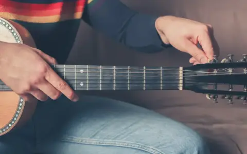 Mężczyzna stroi gitarę 12 strunową, kręcąc kluczem przy główce instrumentu.