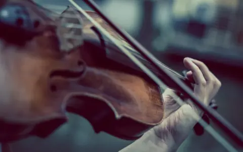 Dłoń gra na skrzypcach Stradivarius, wydobywając z nich magiczne dźwięki.