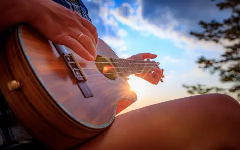 Dłoń z pierścionkiem pokazuje, jak trzymać ukulele, grając przy zachodzącym słońcu.