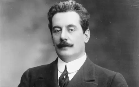 Portret Giacomo Pucciniego, kompozytora operowego, z charakterystycznymi wąsami i w eleganckim garniturze.