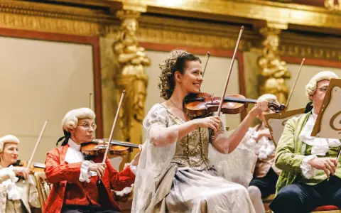 Koncert w stylu epoki Mozarta. W centrum uśmiechnięta kobieta grająca na skrzypcach, przypominająca żonę Mozarta.