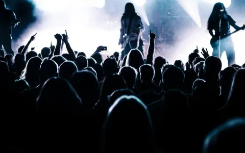 Tłum szaleje na koncercie, ręce w górze, światła sceny tworzą atmosferę legendy historii rocka.