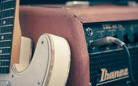 Biała gitara elektryczna podłączona do wzmacniacza Ibanez. Idealny zestaw, by zacząć naukę, jak grać na gitarze elektrycznej.