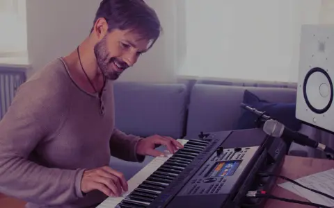 Uśmiechnięty mężczyzna gra na keyboardzie Yamaha, korzystając z aplikacji yamaha flowkey. Obok stoi mikrofon i głośnik.