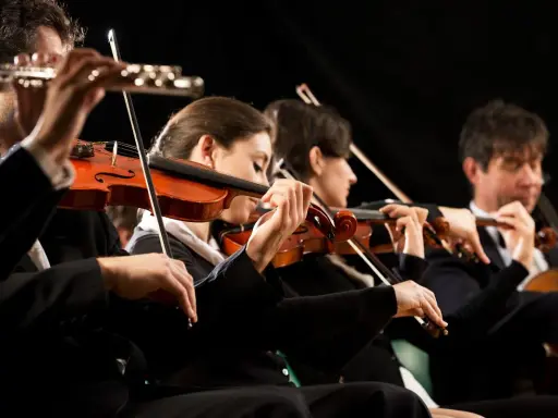 Orkiestra wykonuje utwór jednego z kompozytorów XX wieku. Skupieni muzycy grają na skrzypcach i wiolonczeli.