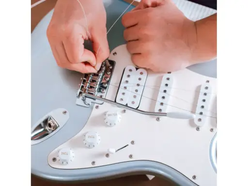 Ręce montują struny do mostka gitary elektrycznej. To ważny krok, jak zrobić gitarę elektryczną, by brzmiała idealnie.