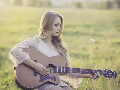 Dziewczyna gra na gitarze, tworząc piękny riff. Słońce delikatnie oświetla jej blond włosy i koronkową sukienkę.