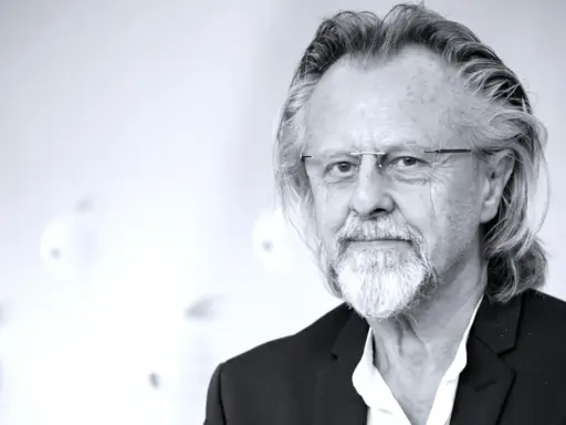 Portret mężczyzny z siwą brodą i długimi włosami, w okularach. Jeden z najlepsi współcześni kompozytorzy.
