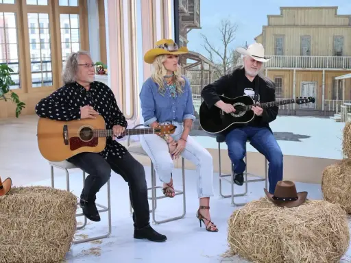 Trzech muzyków gra na gitarach, tworząc muzykę country. W tle stylizowana scenografia z Dzikiego Zachodu.