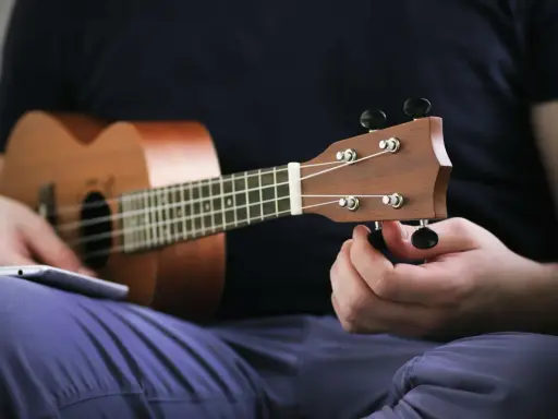 Osoba stroi ukulele, korzystając z aplikacji do nauki gry.