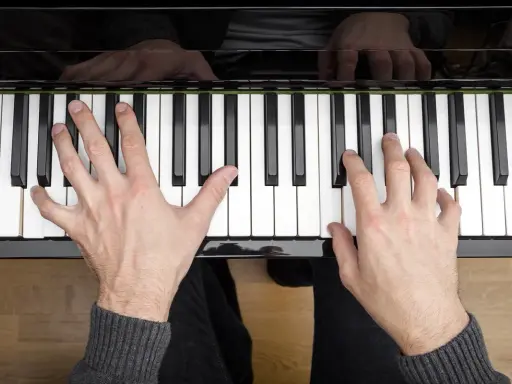 Dłonie grające akordy na pianinie. Muzyka płynie z klawiszy.