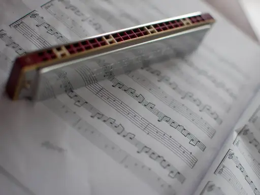 Harmonijka ustna spoczywa na kartach z nutami, gotowa do zagrania melodii.
