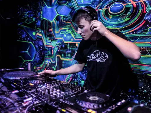 Młody DJ w słuchawkach miksuje muzykę na tle psychodelicznej, neonowej ściany. Chcesz wiedzieć, jak zostać DJ-em? Zacznij od tego!
