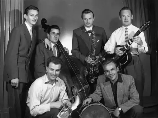 Zespół młodych muzyków, być może najsłynniejsi przedstawiciele jazzu, pozuje z instrumentami: kontrabasem, saksofonem, gitarą i perkusją.