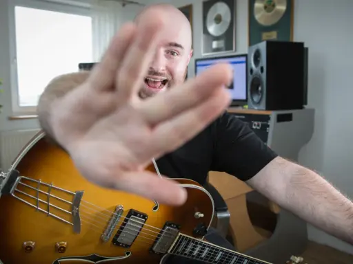 Muzyk z gitarą jazzową, z ręką na pierwszym planie, śpiewa, wyjaśniając, akord co to.
