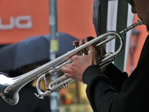 Muzyk gra na trąbce, tworząc dźwięki blues muzyka. W tle deszcz i parasol.