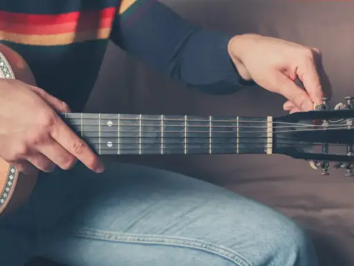 Mężczyzna stroi gitarę 12 strunową, kręcąc kluczem przy główce instrumentu.