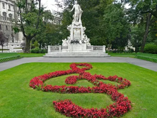 Pomnik Mozarta w Wiedniu, z kluczem wiolinowym ułożonym z czerwonych kwiatów na trawniku.