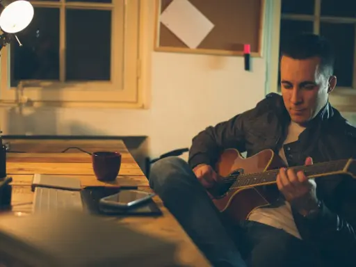 Mężczyzna gra na gitarze, ćwicząc skale gitarowe przy biurku.