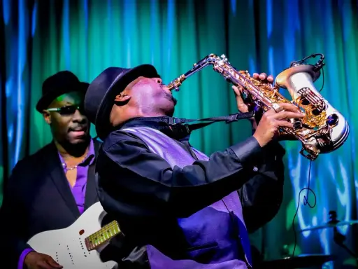 Muzyk gra na saksofonie, tworząc nowoczesny jazz. W tle widać gitarzystę.