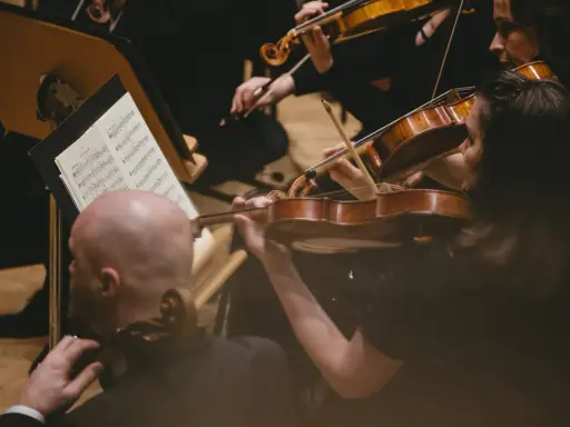 Skupieni muzycy grają na skrzypcach podczas części koncertu bez solisty. Nutki na pulpicie wskazują melodię.