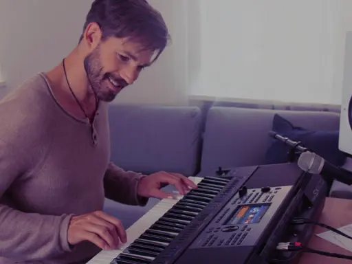 Uśmiechnięty mężczyzna gra na keyboardzie Yamaha, korzystając z aplikacji yamaha flowkey. Obok stoi mikrofon i głośnik.