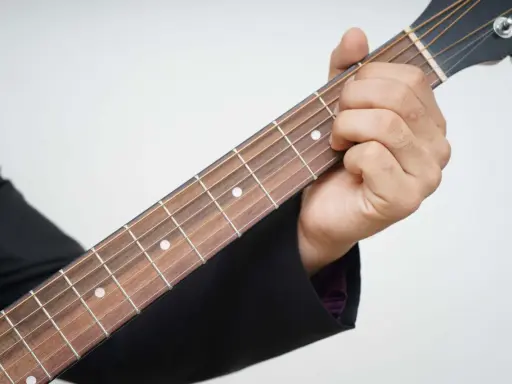 Dłoń dociska struny na gryfie gitary, pokazując pierwszy krok, jak nauczyć się grać na gitarze.